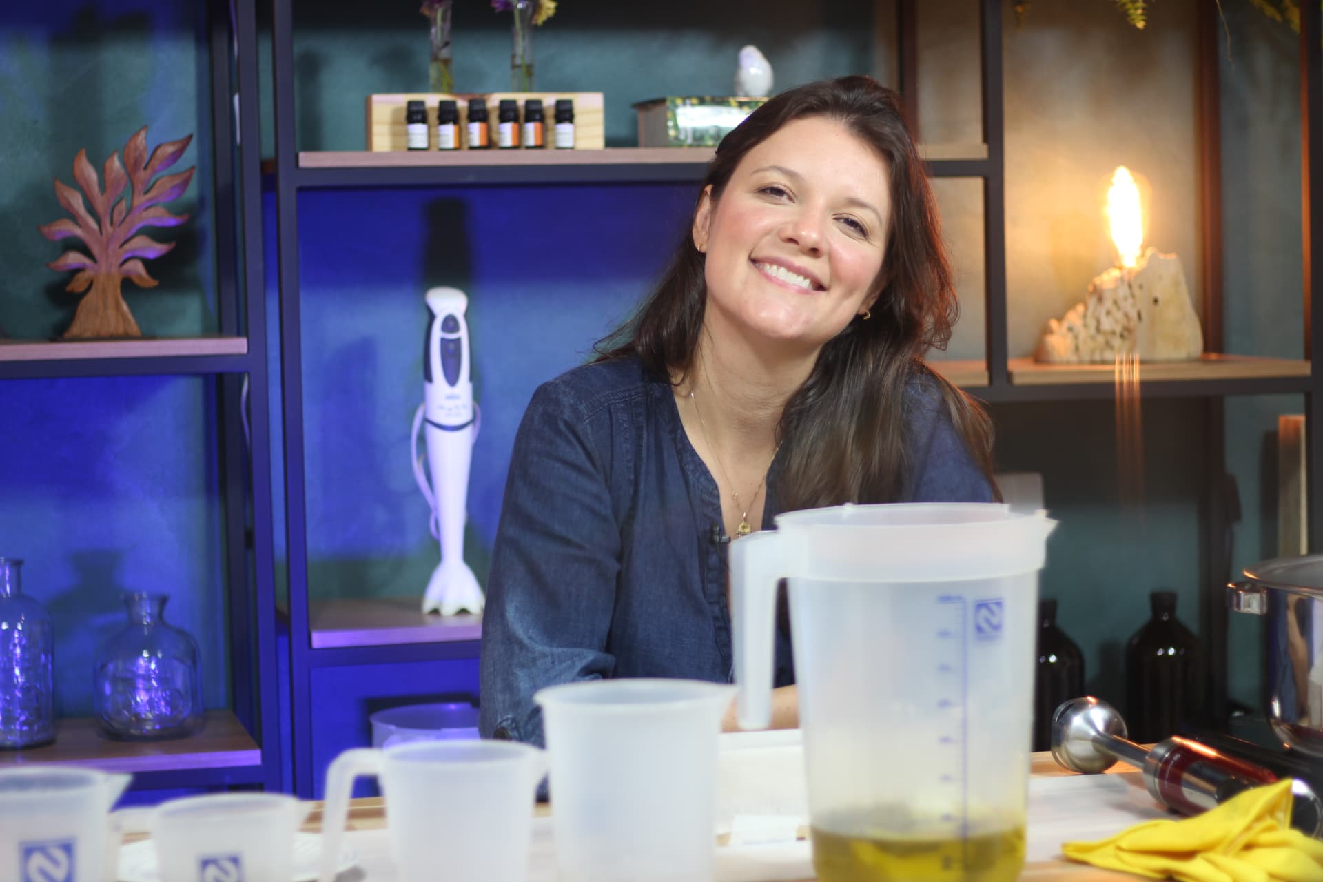 Natália Bisson em seu ateliê de saboaria natural, sorrindo entre ingredientes e ferramentas de produção artesanal
